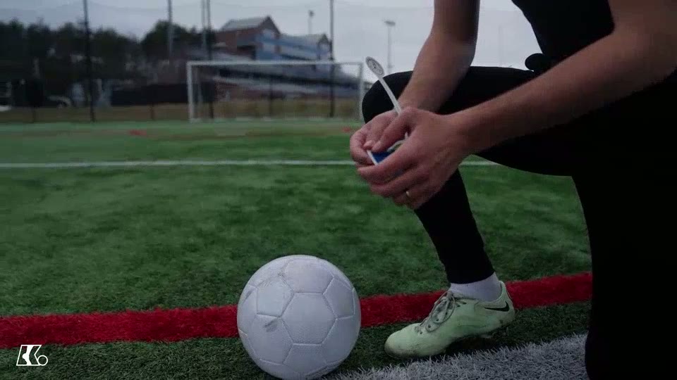 A soccer ball on a grass pitch with a player preparing contact guidance beside a goal.